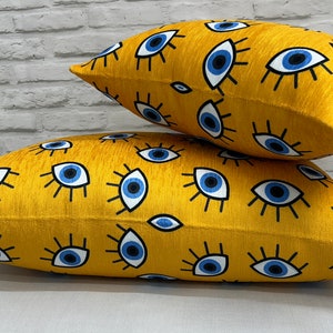 May include: Two yellow throw pillows with a blue eye pattern. The pillows are stacked on top of each other.