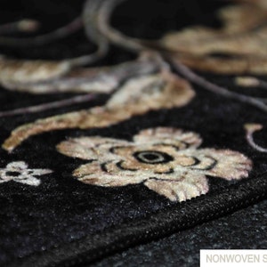 May include: Close-up of a black non-woven soft rug with a floral design in beige and brown. The rug has a subtle sheen and a textured surface.