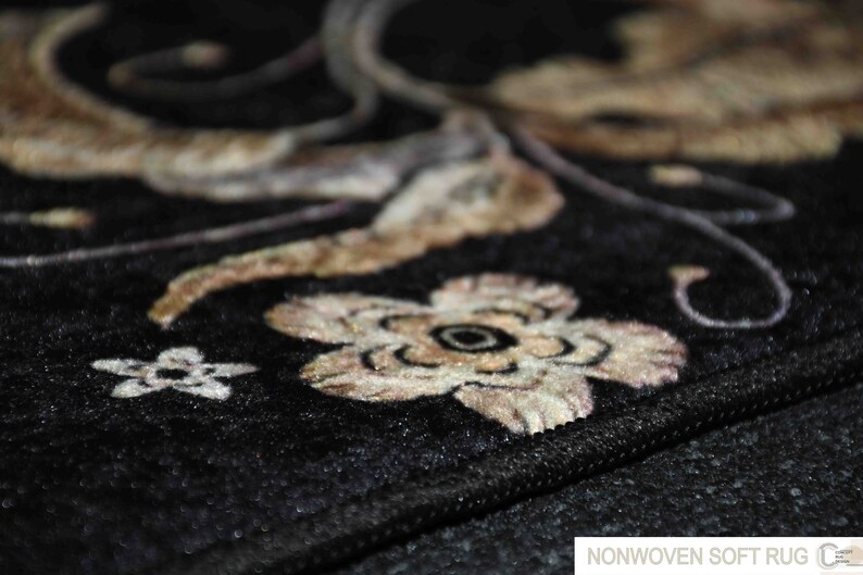 May include: Close-up of a black non-woven soft rug with a floral design in beige and brown. The rug has a subtle sheen and a textured surface.