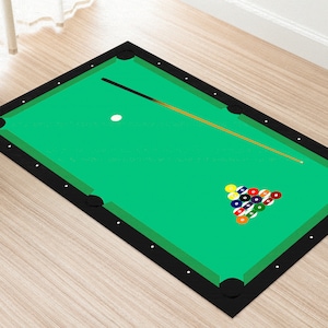 May include: A green felt pool table with black felt edging. The table has a white cue ball and a rack of billiard balls in the lower right corner. A brown pool cue is lying on the table.