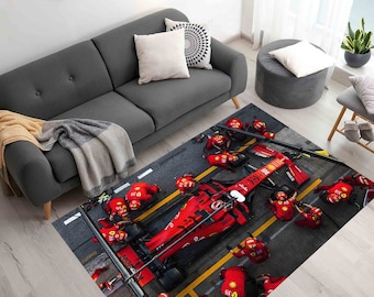 May include: A red race car with black wheels is surrounded by a team of mechanics wearing red jumpsuits. The car is on a gray asphalt surface with yellow lines. The scene is captured on a rug with a racing theme.