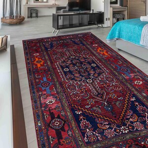 Könnte beinhalten: Ein rechteckiger, gemusterter Teppich mit einem tiefroten Feld und aufwendigen marineblauen und orangefarbenen Designs. Der Teppich weist ein zentrales Medaillon und Bordüren mit geometrischen Mustern auf, geeignet für ein Wohn- oder Schlafzimmer.