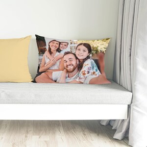 May include: A rectangular pillow with a family portrait, featuring a smiling man, woman, and two children. The pillow is on a gray surface next to a solid yellow pillow. The background includes a white curtain and a wooden floor.