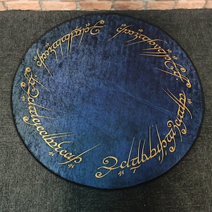 May include: A round blue rug with gold lettering around the edge. The lettering reads "One Ring to rule them all, One Ring to find them, One Ring to bring them all and in the darkness bind them."