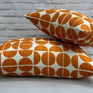 Puede incluir: Dos almohadas de tiro de color naranja y blanco con un diseño geométrico. Las almohadas están apiladas una encima de la otra.