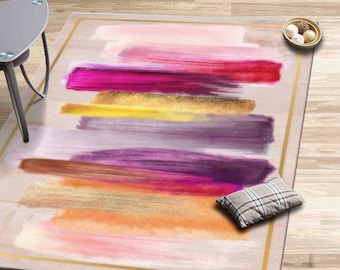 May include: Abstract area rug with a beige background and colorful brushstrokes in shades of pink, purple, orange, yellow, and gold. The rug has a gold border.
