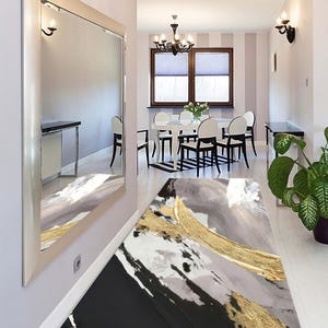 May include: An abstract art runner rug with a black, gray, and gold color scheme. The rug features a modern design with brushstroke-like patterns. The rug is placed in a hallway with a large mirror and a dining area visible in the background.