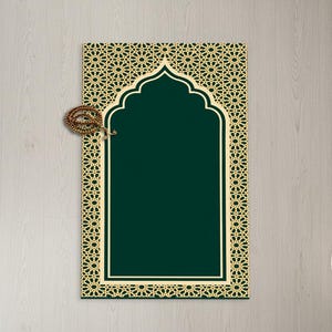 Peut inclure: Un tapis de prière vert avec une bordure géométrique beige et un motif en forme d'arche. Un chapelet repose sur le tapis. Le tapis est rectangulaire et posé sur une surface en bois clair. Une petite plante en pot et un panier tressé sont en arrière-plan.