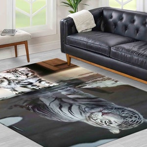 Puede incluir: Una alfombra rayada gris y blanca con un tigre blanco y un gato atigrado sobre ella. La alfombra está sobre un suelo gris claro delante de un sofá de cuero negro.