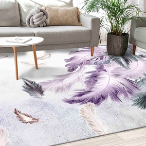 Könnte beinhalten: Ein weißer Teppich mit einem Design aus lila und grauen Federn. Der Teppich befindet sich in einem Wohnzimmer mit einem weißen Sofa und einem Holz-Couchtisch.