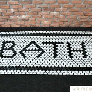 Pode incluir: Tapete de banho de azulejos hexagonais preto e branco com a palavra "BATH" escrita no centro.