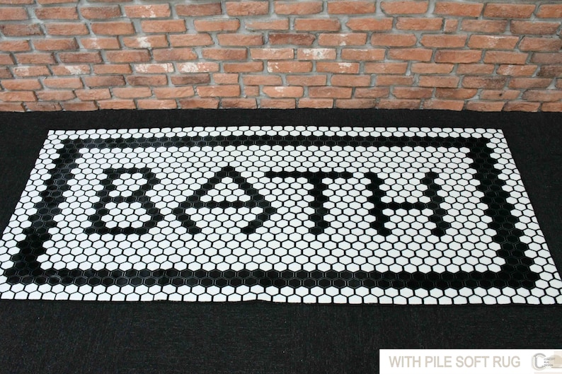 Pode incluir: Tapete de banho de azulejos hexagonais preto e branco com a palavra "BATH" escrita no centro.