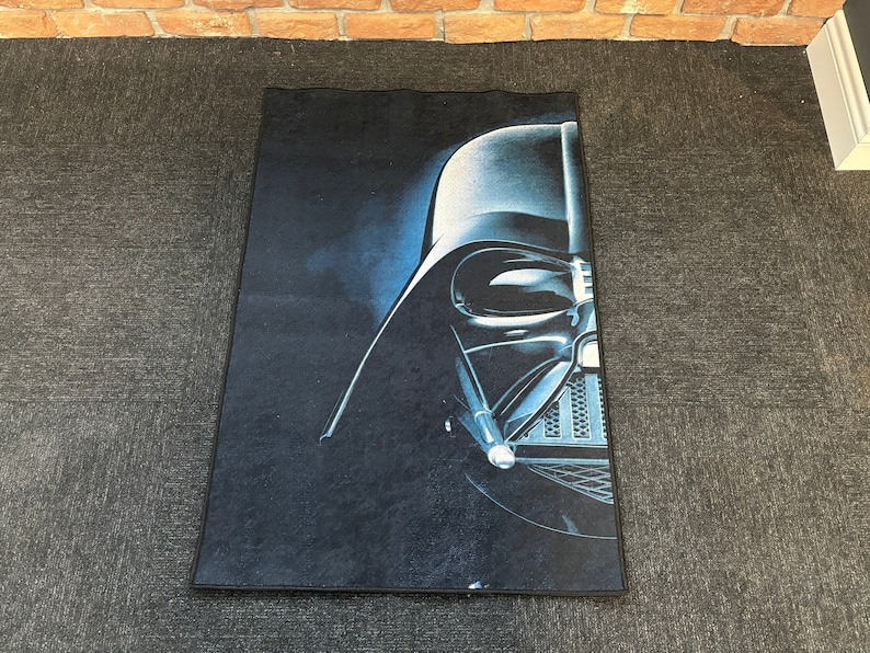 May include: A dark blue rug with a close-up image of Darth Vader's helmet. The helmet is black and silver with a dark blue background.