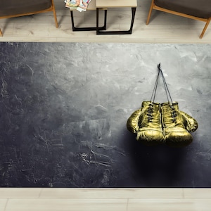 May include: A pair of gold boxing gloves hanging on a gray textured wall.