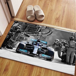 May include: A black and white photo of a Formula 1 race car with a blue and green Petronas logo on the side. The car is being worked on by a team of mechanics in the pit lane.