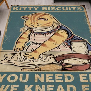 Könnte beinhalten: Eine Vintage-Illustration einer Katze, die Teig knetet, mit dem Text "Kitty Biscuits You Need Em We Knead Em". Die Katze trägt eine rosa-weiße Schürze und hat eine Schüssel mit Teig vor sich.