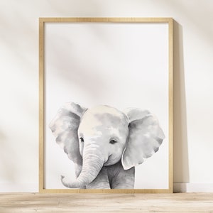 May include: A watercolor painting of a gray baby elephant with large ears. The elephant is looking to the left of the image. The painting is framed in a light wood frame.