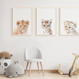 May include: Three framed watercolor paintings of baby animals. The paintings are of a lion, a tiger, and a leopard. The paintings are hung on a white wall in a nursery.