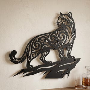 May include: A black metal wall art piece featuring a stylized tiger silhouette with intricate swirling cut-out patterns. The tiger is depicted standing on a jagged rock formation, facing toward the right with its head turned back.