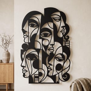 May include: A black metal wall art piece featuring a complex, interconnected composition of multiple stylised human faces with bold, clean lines and geometric shapes. The design displays several overlapping profiles and frontal views.