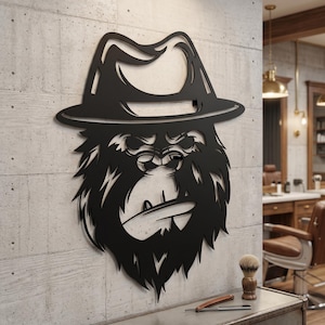 Puede incluir: Una pieza de arte mural de metal negro que presenta una cabeza de gorila estilizada con un sombrero fedora. El diseño está cortado de una sola hoja de metal, mostrando los rasgos faciales del gorila, el pelaje grueso y el ala del sombrero.