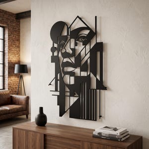 May include: A black metal wall art piece featuring a geometric, abstract portrait of a face. The design is composed of sharp lines, angular shapes, and circular elements that form the eyes, nose, and lips in a stylised, layered composition.