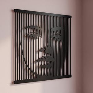 Pode incluir: Uma peça de arte de parede preta com uma série de ripas verticais que formam a imagem em espaço negativo de um rosto humano. O design consiste em barras paralelas finas conectadas por bordas horizontais na parte superior e inferior.