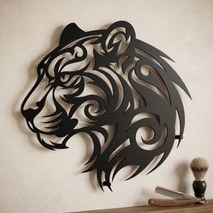 May include: A black metal wall art piece shaped like the profile of a tiger head. The design features intricate cutouts and swirling patterns that form the facial features and fur of the animal. The piece is mounted flat against a light wall.