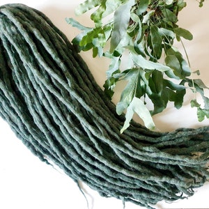 May include: A bundle of dark green wool dreadlocks. The dreadlocks are long and thick, and they are arranged in a loose pile.