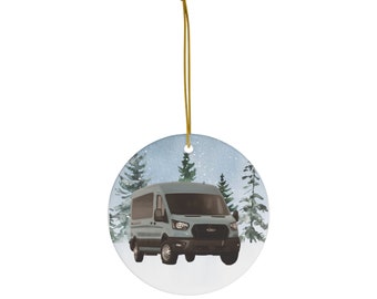 May include: A round ceramic ornament featuring a blue van driving through a snowy forest scene. The van is surrounded by pine trees and the background is a light blue sky with white snowflakes.
