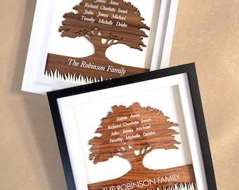 May include: Two square framed wall art pieces featuring a laser-cut wooden tree silhouette. One frame is white, the other black. Each contains a brown wooden tree with names engraved in the canopy and the text The Robinson Family on the trunk base.