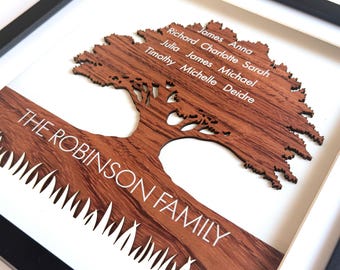 May include: A framed wall art piece featuring a dark wood cutout of a tree with grass at the base. The text THE ROBINSON FAMILY is engraved on the trunk. The names James, Anna, Richard, Charlotte, Sarah, Julia, James, Michael, Timothy, Michelle, Deidre are on the tree canopy.