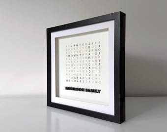 May include: Black and white framed print with a word search puzzle featuring the names "James", "Susan", "Robert", "Mommy", "Daddy", "Sarah", and "Michael". The names are spelled out in a grid of letters. The bottom of the print reads "Robinson Family".