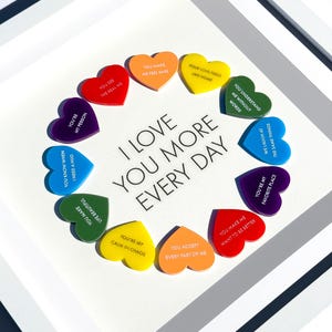 May include: Framed artwork featuring a white background with a ring of colourful heart-shaped cutouts. Each heart displays a unique message, including "You're my person" and "I love you more every day."
