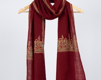 May include: A maroon shawl with a gold embroidered border. The shawl is hanging on a wooden hanger.
