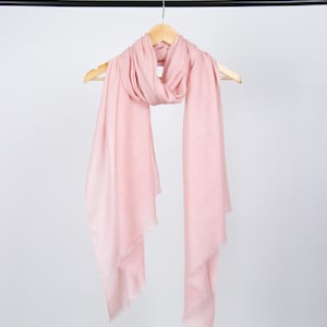 May include: A pale pink scarf with a fringed edge hangs on a wooden hanger against a white background.