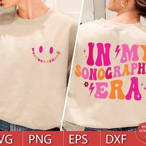Puede incluir: Una sudadera de color beige claro con un gráfico rosa y naranja que dice "In My Sonographer Era" con una carita sonriente en la parte delantera.
