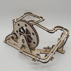 May include: Wooden marble run toy with a large gear and a track that winds around the gear. A small metal ball is visible on the track.