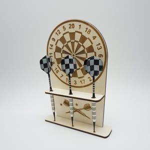 Peut inclure: Un jeu de fléchettes en bois et un support. Le jeu de fléchettes a un design classique avec des chiffres et un centre. Trois fléchettes avec des plumes à carreaux sont dans le support. Le support a une étagère avec un motif de fléchettes croisées.