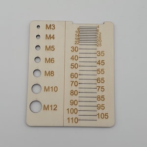 May include: A wooden tool for measuring the diameter of bolts and nuts. The tool has a series of holes for different sizes of bolts and nuts, labelled M3, M4, M5, M6, M8, M10, and M12. The tool also has a ruler on the side, with markings from 4 to 110.