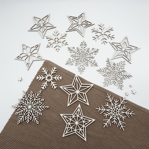 May include: A collection of wooden Christmas ornaments, including star and snowflake shapes. The ornaments are light brown and arranged on a brown textured surface against a white background. Ideal for holiday decor.