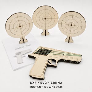 Può includere: Una pistola giocattolo in legno chiaro con elastici verdi, tre bersagli circolari in legno su supporto con reticoli incisi e un foglio di istruzioni con il testo INSTRUCTIONS, DXF, SVG, LBRN2 e INSTANT DOWNLOAD.