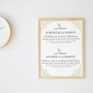 Peut inclure: Un cadre avec des textes arabes et des traductions françaises, avec des motifs d'angle ornés. Le texte comprend des phrases pour sortir et entrer dans une maison. Une horloge ronde avec un cadre doré est visible en arrière-plan.