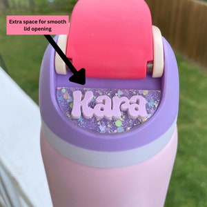May include: A pink and purple water bottle with a clear lid and a personalized name tag that says "Kara". The lid has a pink flip top with extra space for smooth lid opening.