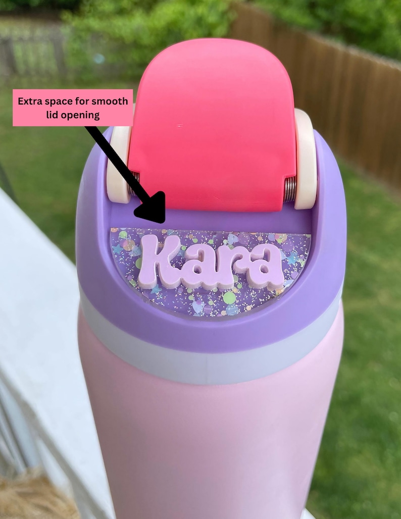 May include: A pink and purple water bottle with a clear lid and a personalized name tag that says "Kara". The lid has a pink flip top with extra space for smooth lid opening.