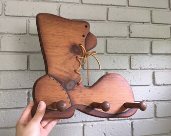 May include: Wooden boot-shaped coat rack with three hooks. The boot is painted brown with a brown leather lace detail.