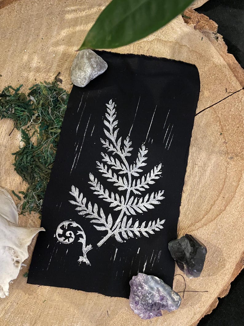 May include: A black fabric print with a silver fern design. The print is on a black background and features a fern with a curled frond.