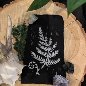 May include: A black card with a silver fern design printed on it. The card is surrounded by small stones and a deer antler.