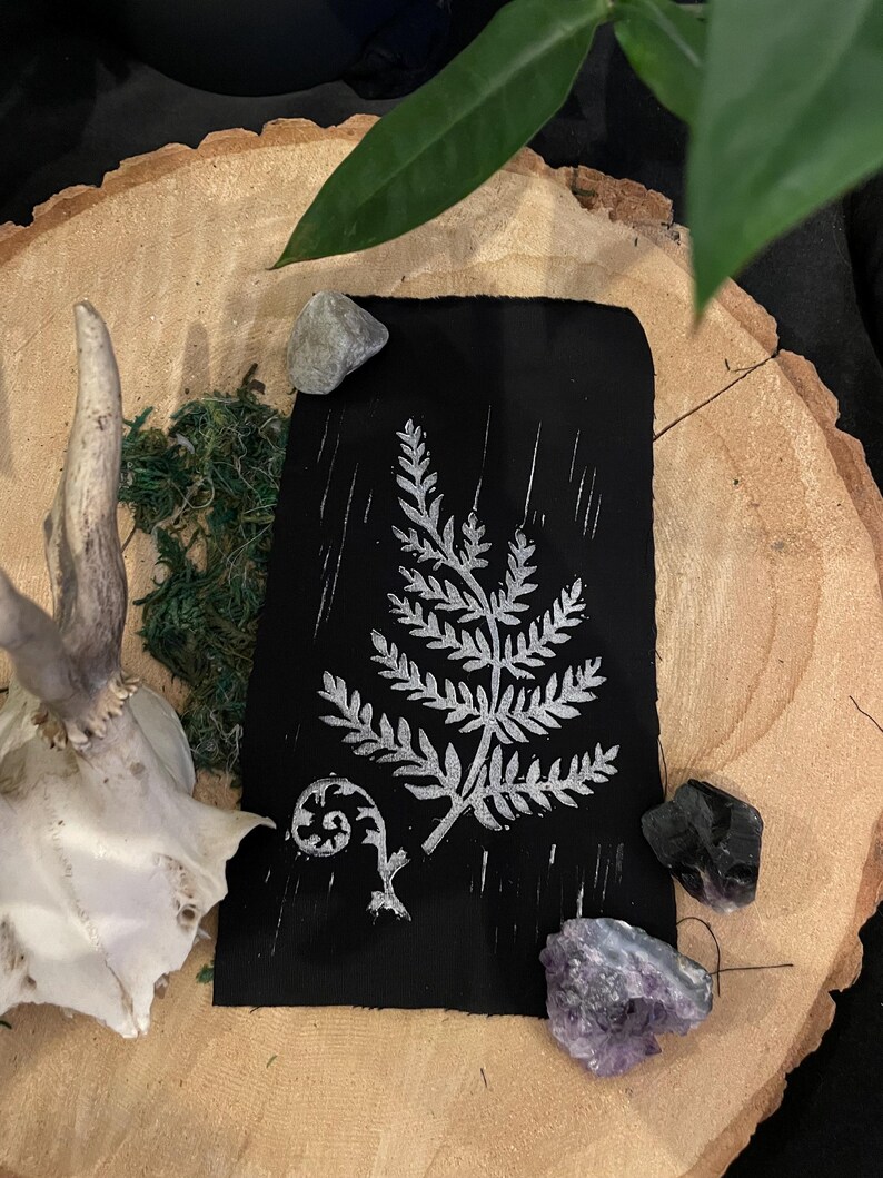 May include: A black card with a silver fern design printed on it. The card is surrounded by small stones and a deer antler.