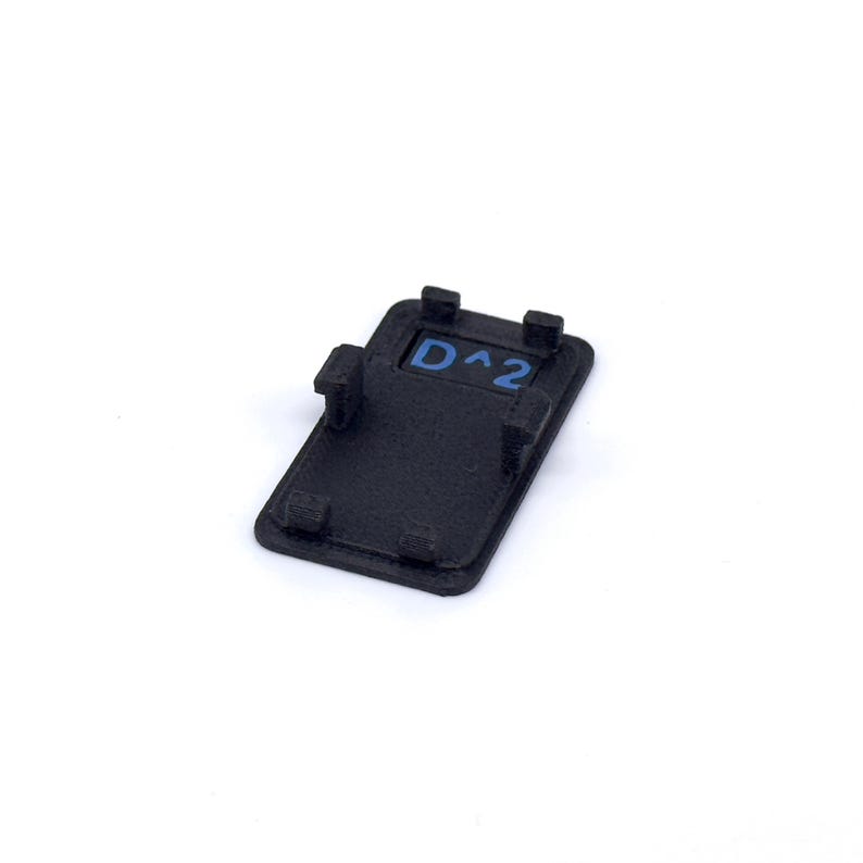 May include: Black plastic button with a blue inscription that reads "D^2".